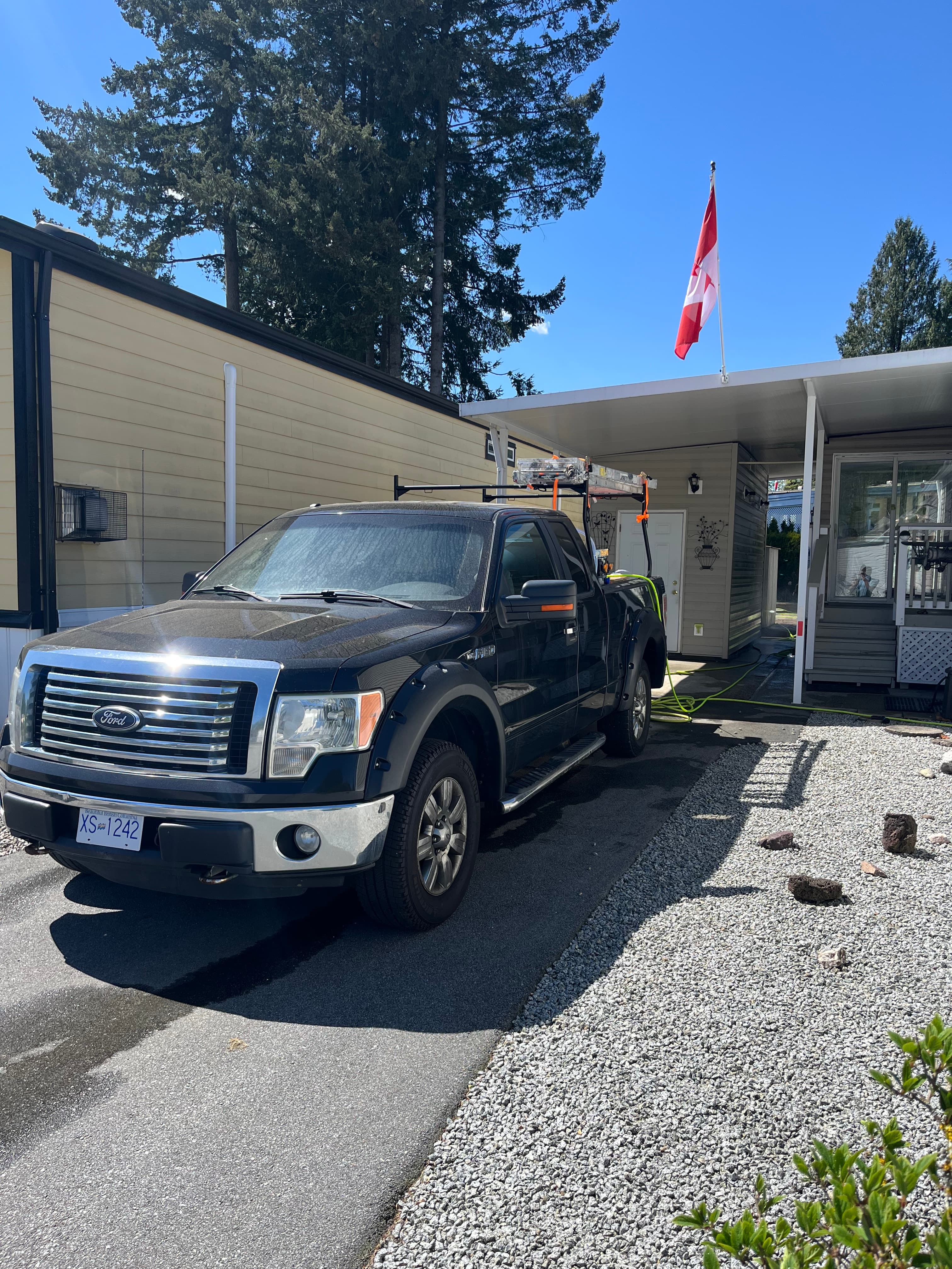 Black Ford pickup truck parked in a driveway beside a house with a Canadian flag.